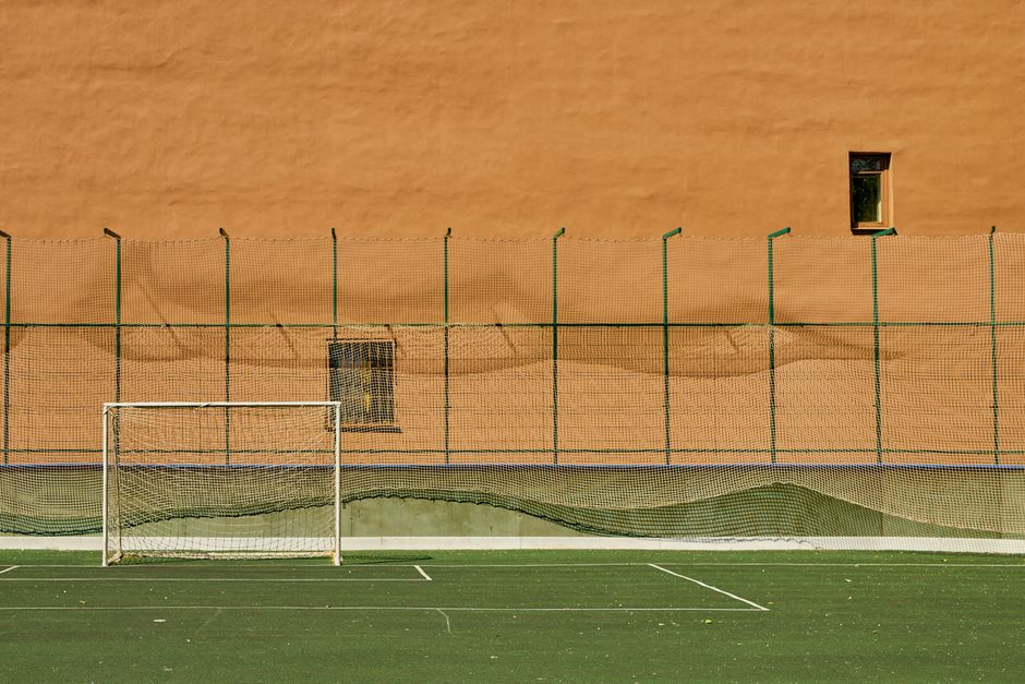 A solitary soccer goalpost stands in an empty sports ground with a vibrant wall backdrop.