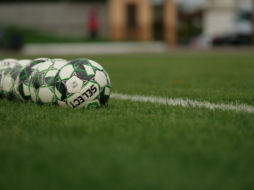 Close-up view of soccer balls lined up on a grassy football field.