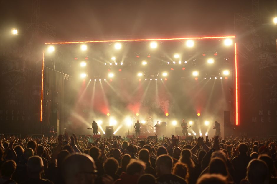 Dynamic live concert with band on stage, lighting effects, and enthusiastic crowd at night.