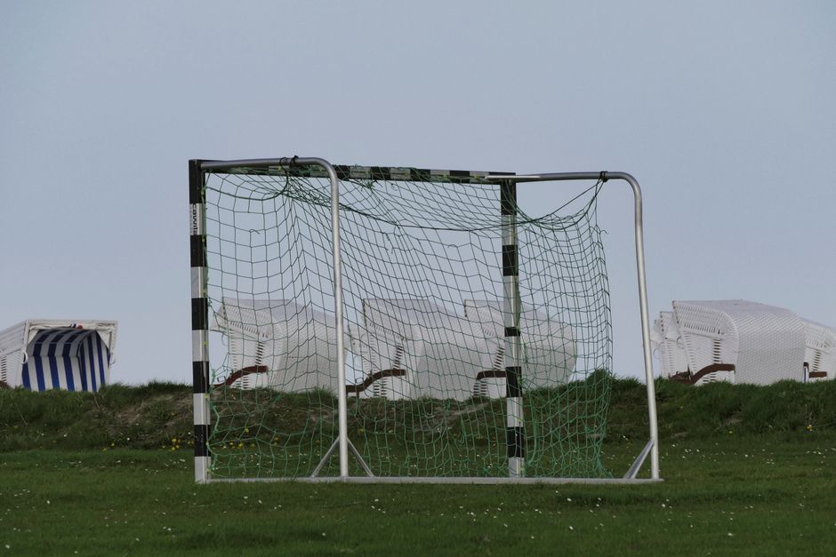 Empty soccer goal on a grassy field with wicker beach chairs in the background, serene outdoor setting.
