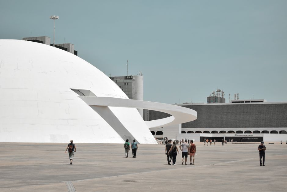 Visitors explore the futuristic exterior of Brasilia's iconic National Museum in daylight.