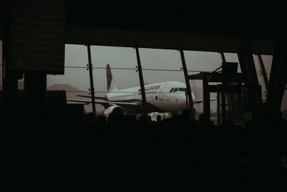 Silhouette of an airplane and waiting passengers inside an airport terminal at dusk.
