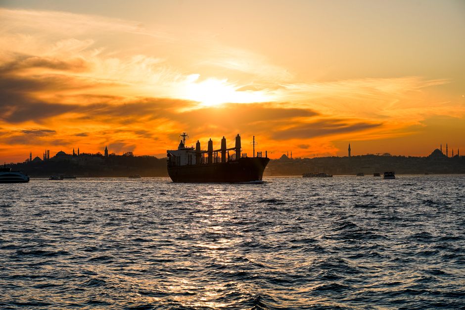 Cargo ship on Bosphorus at sunset with Istanbul's skyline creating a dramatic silhouette.