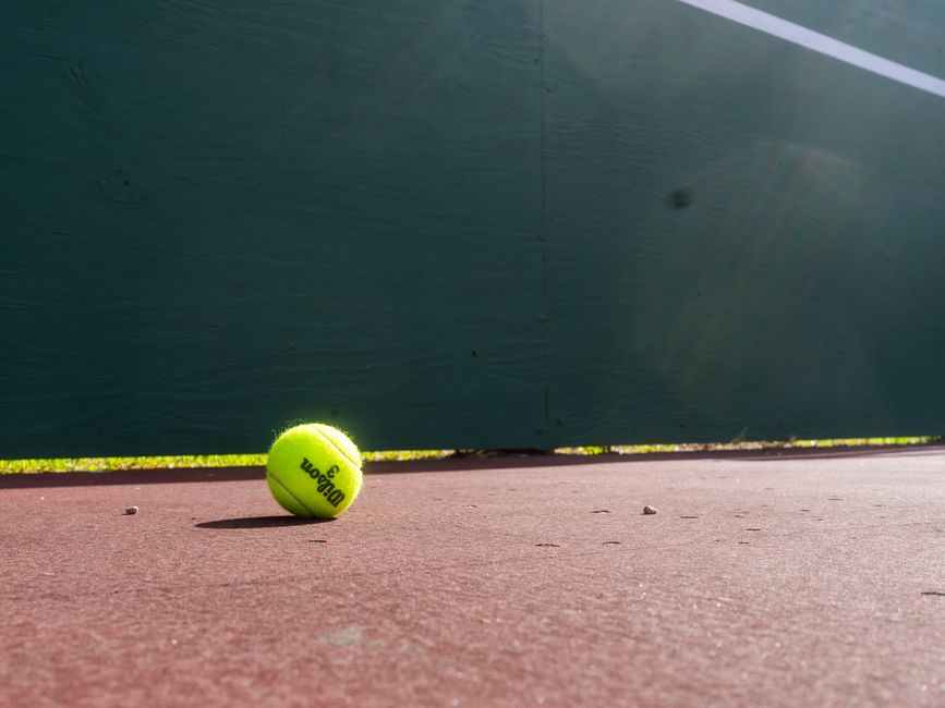 Vibrant tennis ball resting on a court in Houston, showcasing sunlight and shadows.