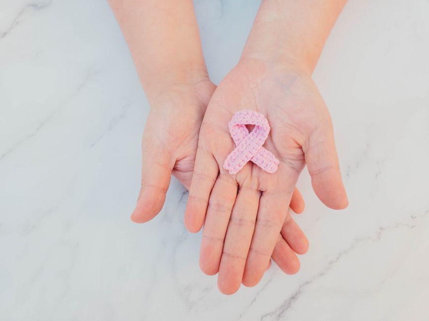 Pink ribbon in hands symbolizing breast cancer awareness on marble background.