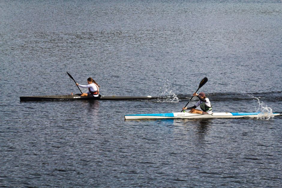 Two athletes paddle fiercely in a kayak race on a calm lake, showing competitive spirit and agility.