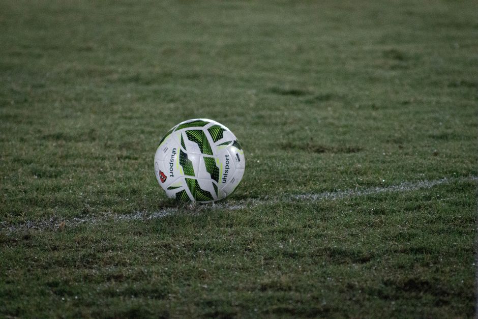 A soccer ball resting on a grass field, captured during nightfall with visible dew.