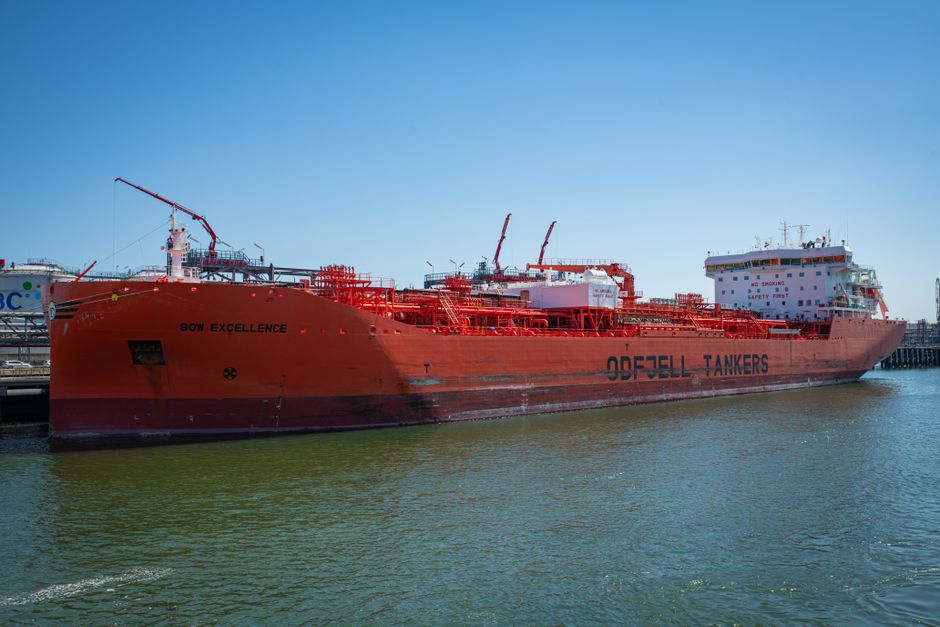A large red oil tanker named Bow Excellence docked at a harbor under clear blue skies.