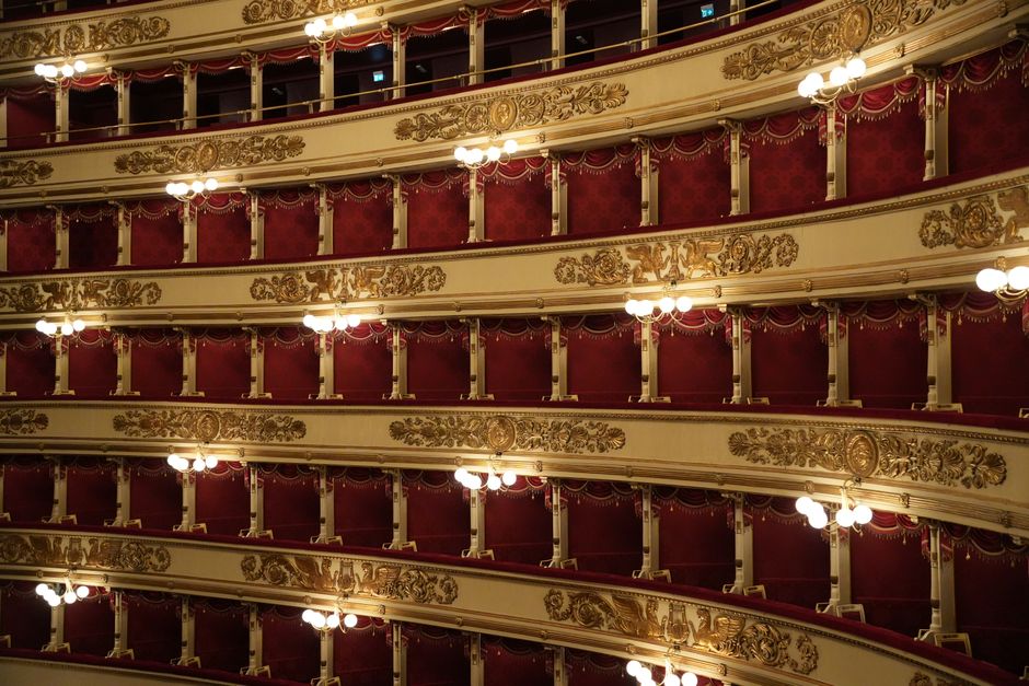 Detailed view of ornate balconies in a historic opera house in Italy, showcasing intricate design and vibrant red decor.