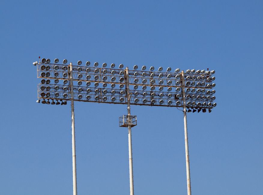 Tall stadium floodlights towering against a clear blue sky, perfect for outdoor sports lighting visuals.