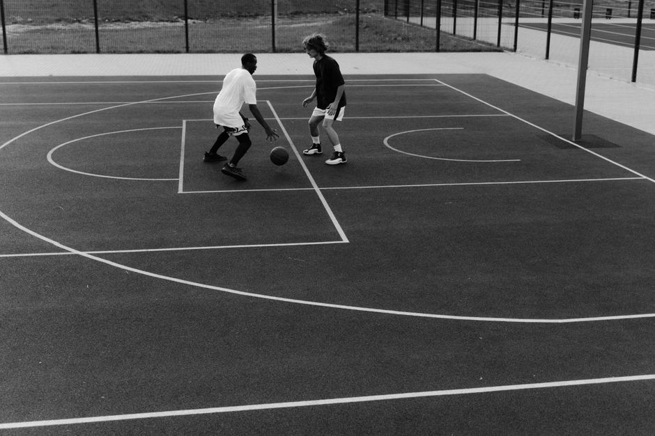 Two men playing basketball on an outdoor court in a black and white photograph.