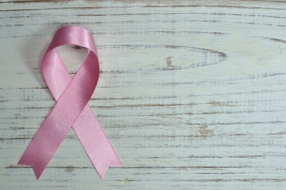 A pink ribbon symbolizing cancer awareness placed on a light wooden background.