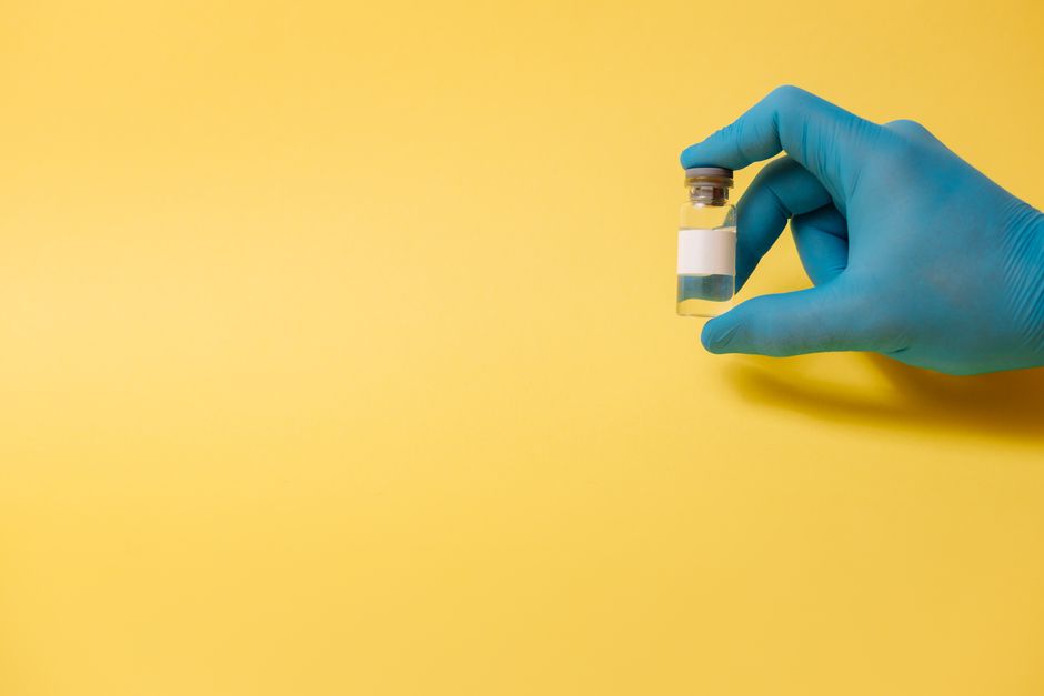 A gloved hand holds a medical vial against a bright yellow background, symbolizing health and medicine.