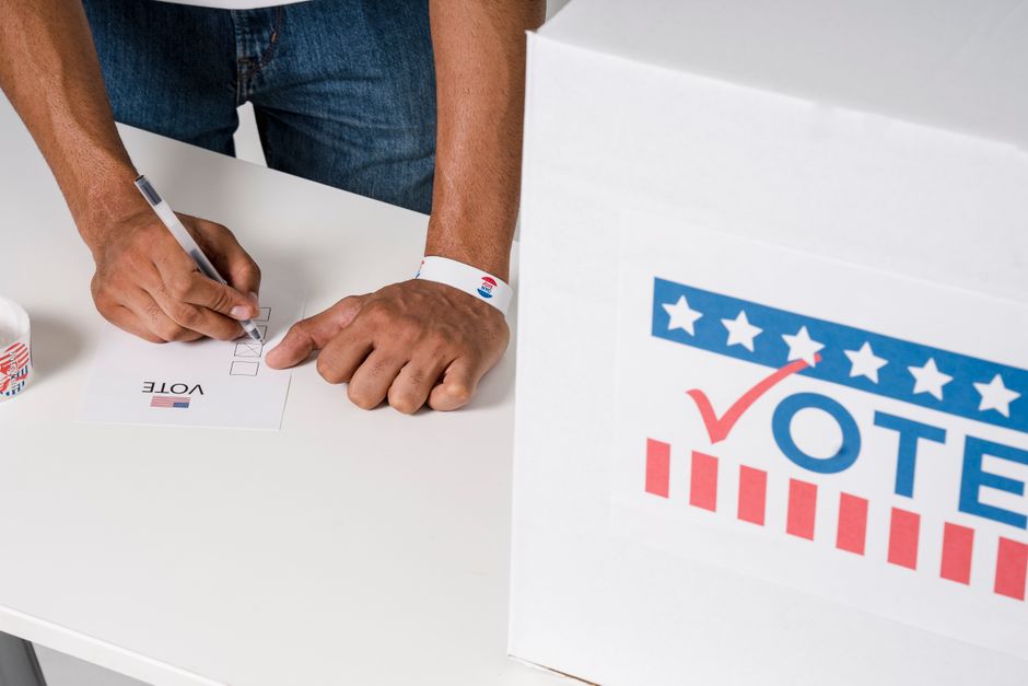 A person casting a vote with a ballot near a marked voting box, emphasizing civic participation.