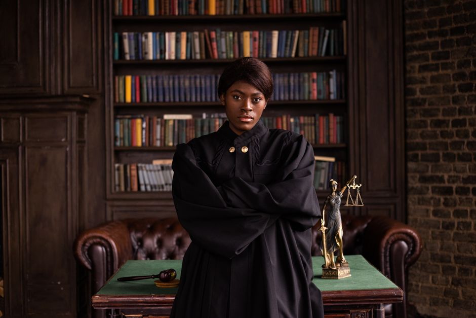 A confident female judge in a formal robe posing in a classic legal library setting.