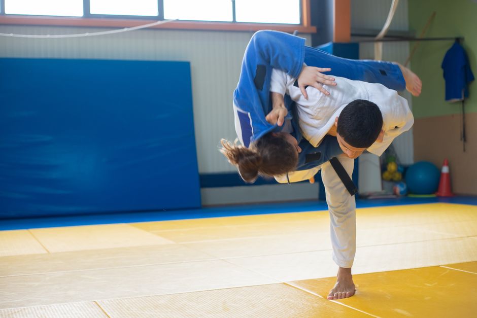 Two judokas practicing a powerful throw during judo training indoors on tatami mats.