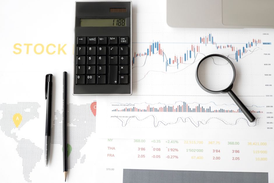 Flat lay of stock market analysis tools including calculator, graphs, and magnifying glass.
