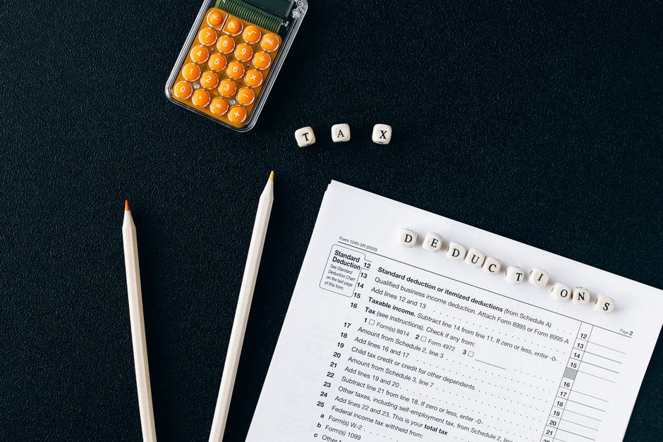 Flat lay of tax form, pencils, and calculator on black background, emphasizing tax deductions.