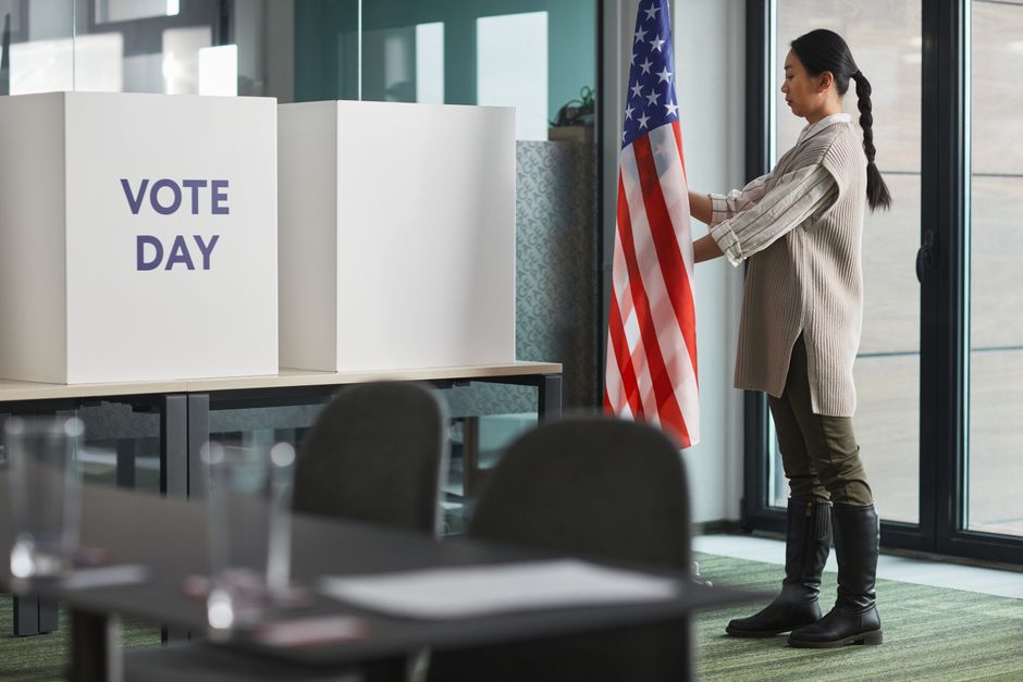 Woman standing near American flag and ballot boxes during voting day