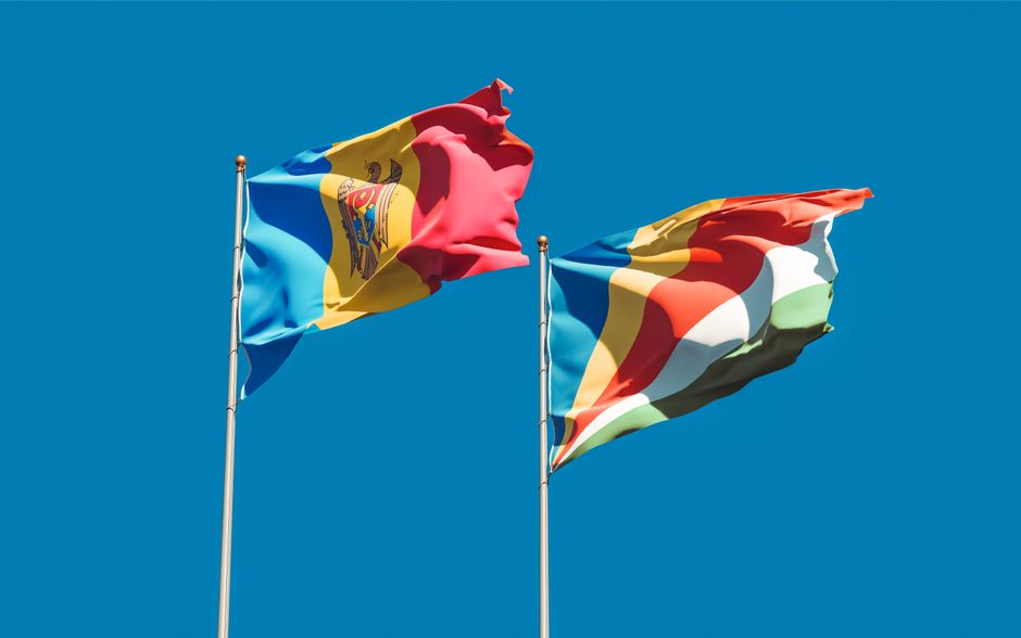 Seychelles and Moldova flags waving on flagpoles against a clear blue sky, symbolizing national pride.