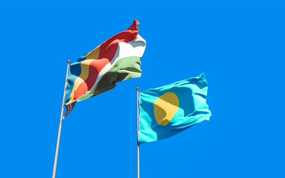 Two national flags waving in the wind against a clear blue sky, representing Seychelles and Palau.