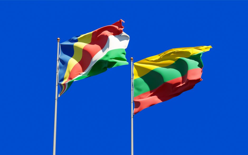 Colorful flags of Seychelles and Lithuania waving under a clear blue sky.