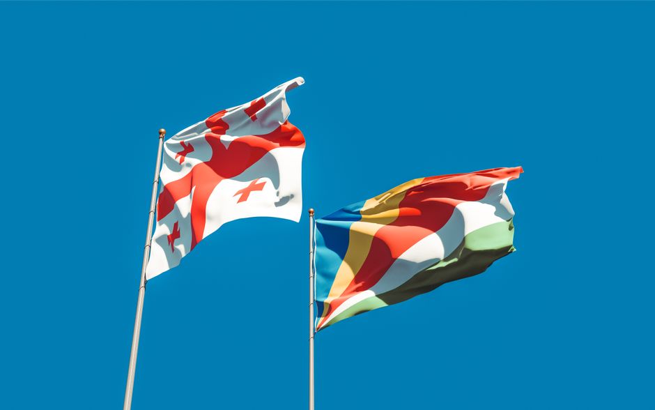 Vibrant image of Georgia and Seychelles flags waving with blue sky backdrop, symbolizing unity and cultural pride.