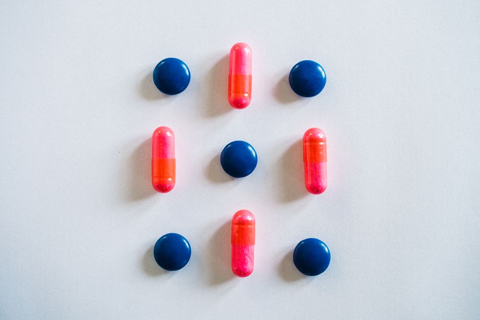 A top-down view of blue and pink pills and capsules arranged on a white background.