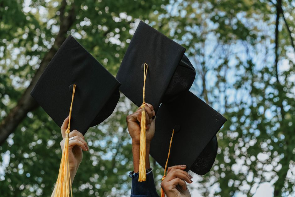 Three hands holding graduation caps in celebration, symbolizing success.