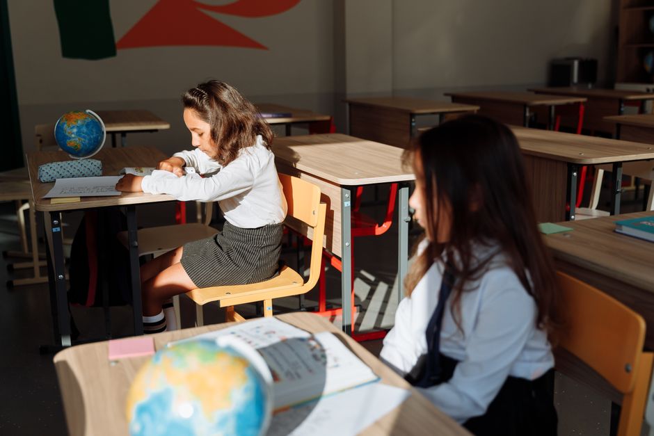 Two young girls focused on their studies in a sunlit classroom with a globe.
