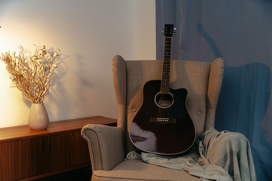 An acoustic guitar placed on a cozy armchair in a warm-lit living room setting.